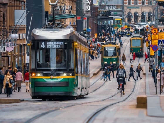 Raitiovaunuja ja ihmisiä Helsingin vilkkaalla keskustakadulla, taustalla vanhoja rakennuksia.