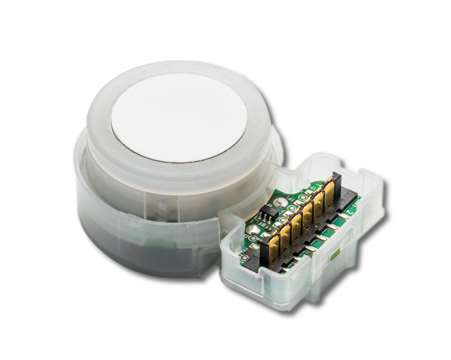 Rund elektronisk sensor med vit topp och exponerade guldkontakter på ett grönt kretskort.