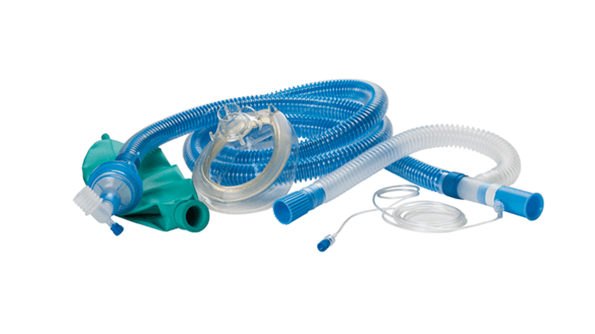 Sinivalkoinen lääkinnällinen hengityslaite, jossa on maski, letkuja ja vihreä säiliöpussi, valkoisella taustalla.