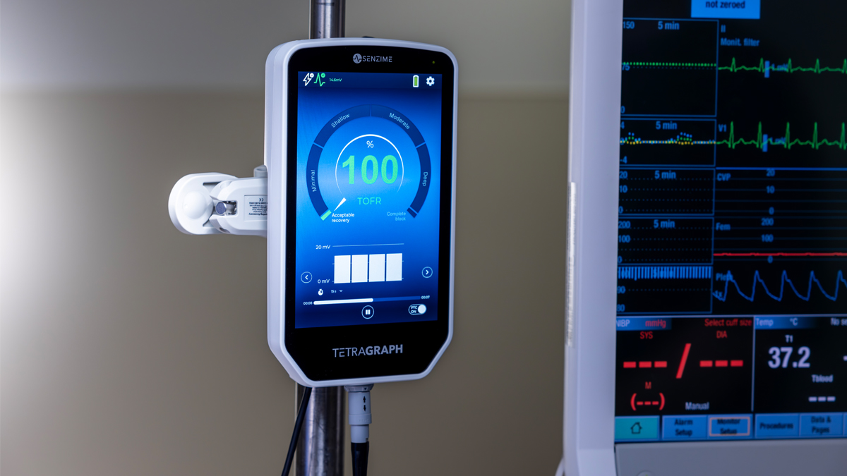 Närbild av en medicinsk monitor som visar "100%" och andra avläsningar, bredvid en annan skärm som visar vitala tecken.