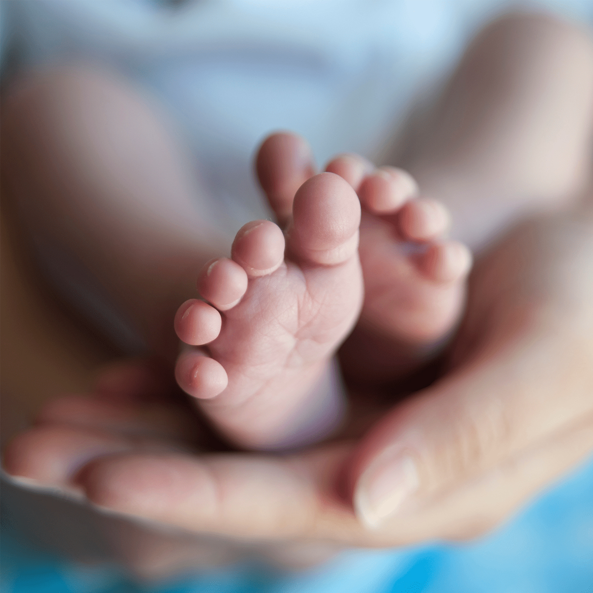 Vauvan pienet paljaat jalat aikuisen käsissä, tausta on sumea.