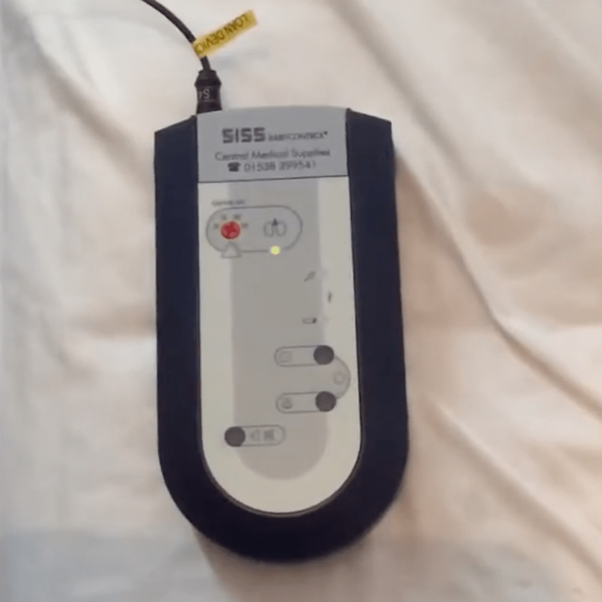 Sähköinen lääkintälaite valkoisella kankaalla, teippi johdossa ja painikkeet laitteessa.