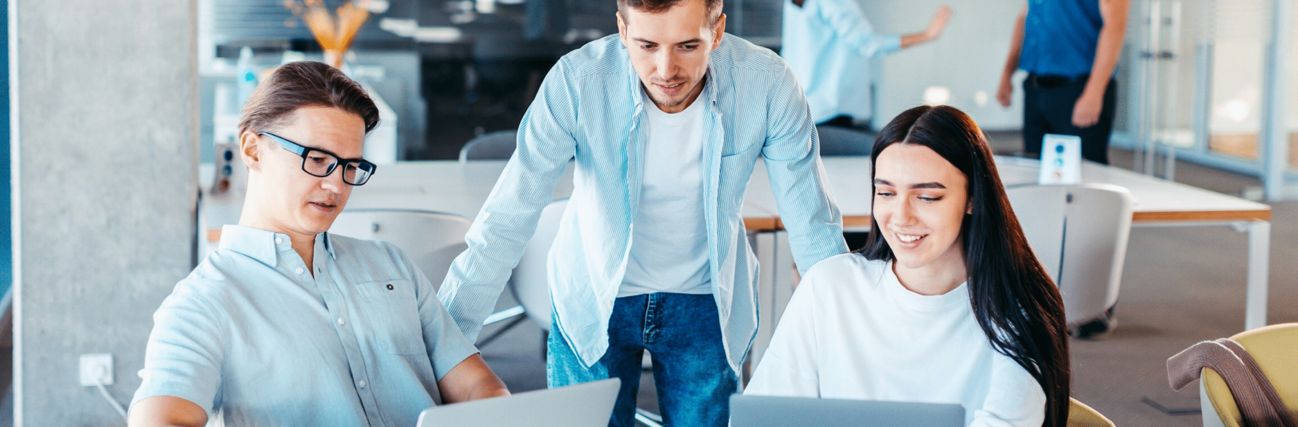 Kolme nuorta ammattilaista työskentelemässä yhdessä kannettavien tietokoneiden ääressä modernissa toimistotilassa.